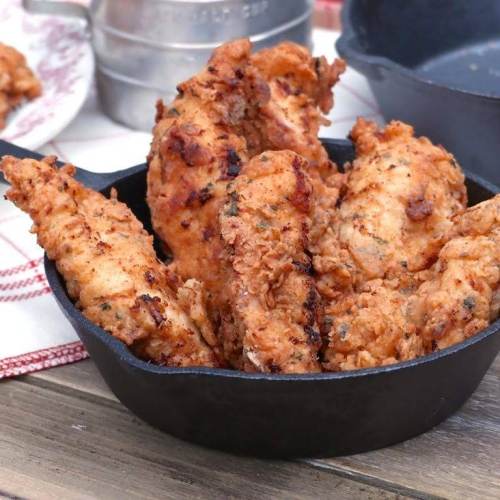 Crispy fried chicken tenders served in a cast iron skillet on a rustic wooden table.