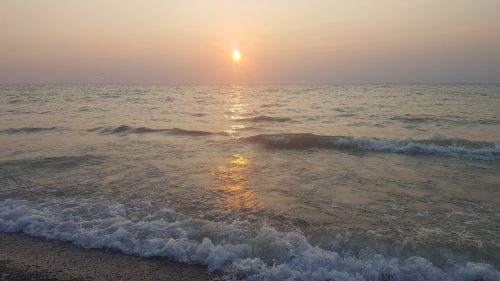 Sunset over a calm sea, with gentle waves lapping at the shore and a warm golden glow reflecting on the water.