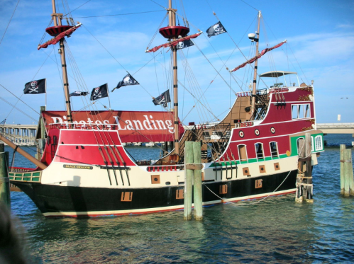 A colorful pirate ship docked in the water, featuring black flags with skulls and the name "Pirates Landing."