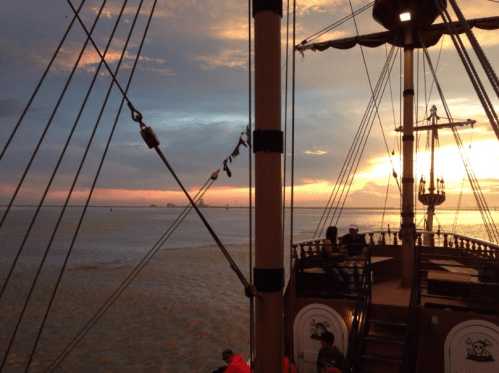 A ship's deck with ropes and a sunset over the water, creating a serene maritime atmosphere.
