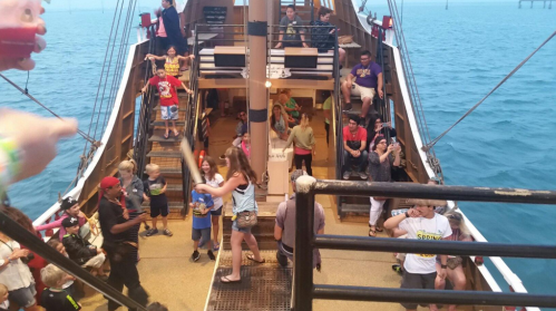 A lively scene on a ship with children and adults enjoying activities on deck, surrounded by water.