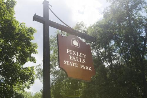 Sign for Pixley Falls State Park surrounded by trees and a cloudy sky.