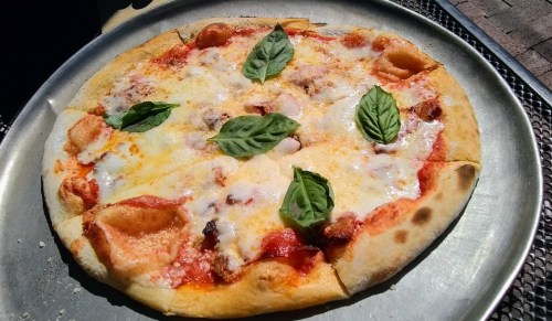 A freshly baked pizza topped with melted cheese, tomato sauce, and fresh basil leaves on a metal tray.
