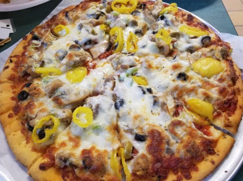 A freshly baked pizza topped with cheese, mushrooms, olives, green peppers, and yellow peppers on a golden crust.