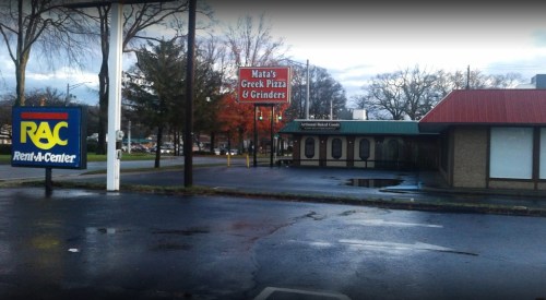 A street view featuring a Rent-A-Center sign and Mata's Greek Pizza & Grinders restaurant with a cloudy sky.