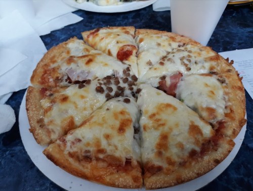 A freshly baked pizza with melted cheese, pepperoni, and sausage, sliced into eight pieces on a white plate.