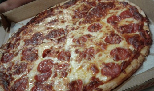 A large pepperoni pizza with melted cheese, partially sliced, in a cardboard pizza box.