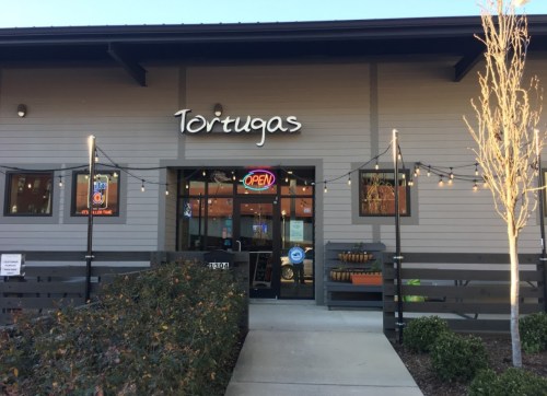 Exterior of Tortugas restaurant with an "OPEN" sign, string lights, and a landscaped entrance.