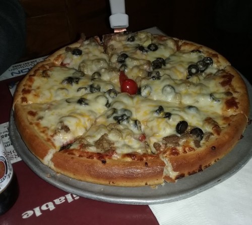 A delicious pizza topped with cheese, olives, and a cherry tomato, served on a metal tray.