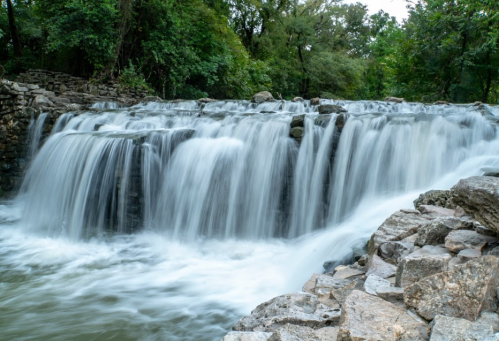 A serene waterfall cascading over rocks, surrounded by lush greenery and a tranquil river below.