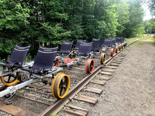 A row of pedal-powered rail bikes lined up on a railway track surrounded by greenery.