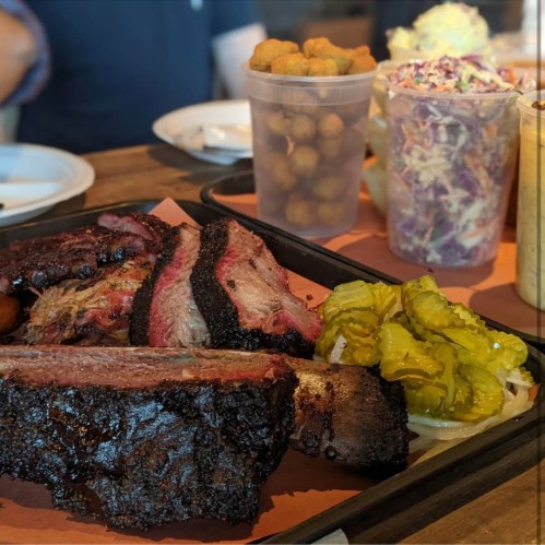A platter of smoked meats, including brisket and ribs, served with pickles, coleslaw, and a side of fried okra.