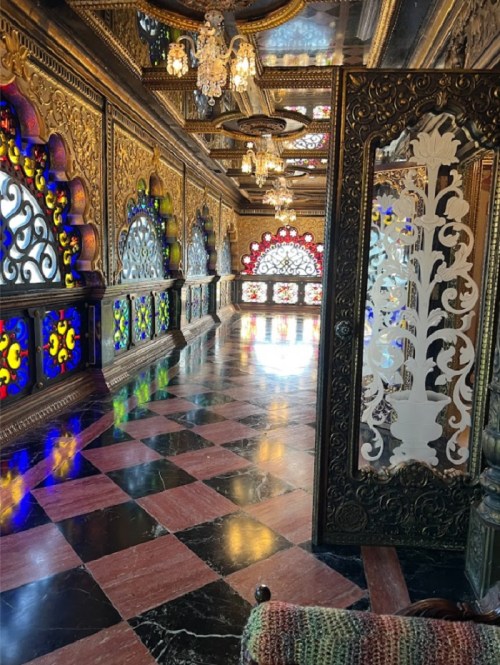 Ornate interior with colorful stained glass windows, intricate gold detailing, and a polished marble floor.