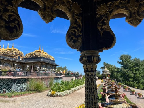 A view of ornate architecture with golden roofs and lush gardens under a clear blue sky.