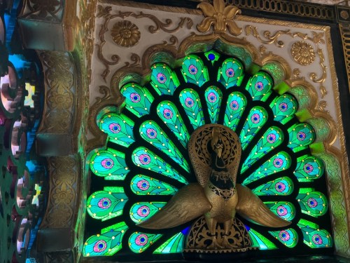 A vibrant peacock design with intricate green and blue patterns, set against a gold and white background.