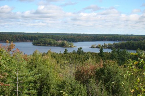 A scenic view of a lake surrounded by lush green forests and a cloudy sky.