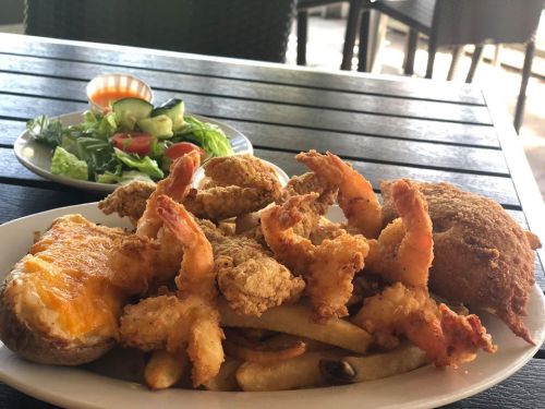 A plate of fried shrimp, chicken, and fries, with a side salad of mixed greens and tomatoes.