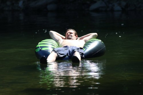 A man relaxes on a green and black inflatable tube in calm water, enjoying a sunny day.