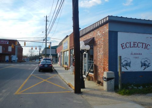 A street view of Eclectic, Alabama, featuring brick buildings, a traffic light, and a parked car.