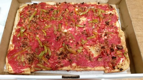 A rectangular pizza topped with red sauce, green peppers, and sausage, in a cardboard box.