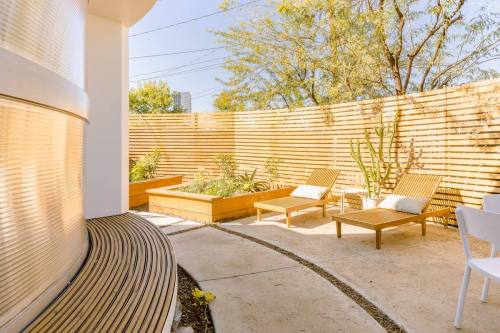 A sunny outdoor space with wooden fencing, lounge chairs, and garden beds surrounded by greenery.