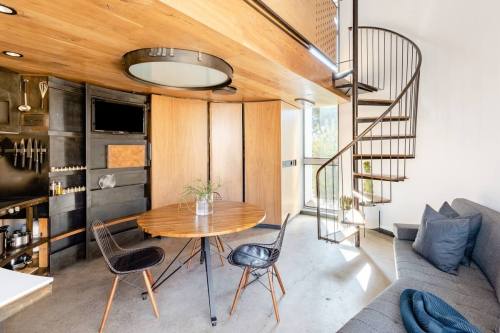 Modern interior featuring a round wooden dining table, black chairs, a spiral staircase, and a cozy sofa in a bright space.