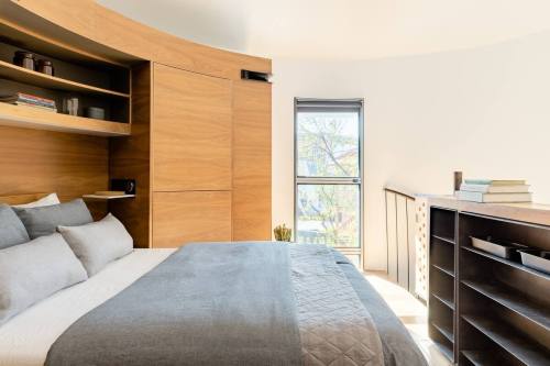 Cozy bedroom with wooden furniture, a large window, and a neatly made bed featuring gray linens.