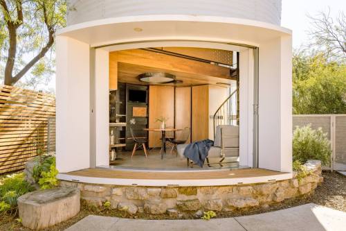A modern, circular building with large sliding doors, featuring a cozy interior and outdoor seating area.