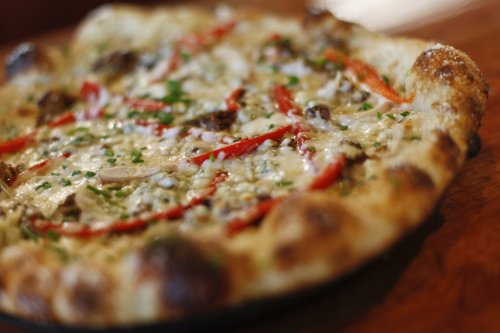 A close-up of a freshly baked pizza topped with cheese, red peppers, and herbs on a wooden table.