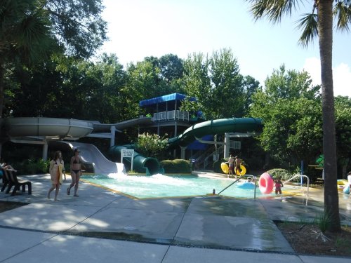A water park scene featuring slides, a pool, and people enjoying the sun on a clear day.