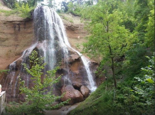 A cascading waterfall flows down a rocky cliff, surrounded by lush green trees and foliage.
