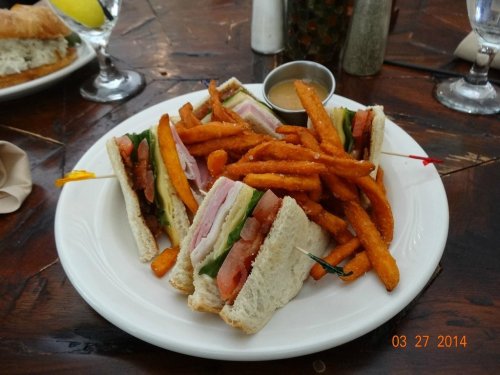 A plate of club sandwiches with lettuce, tomato, and turkey, served with a side of sweet potato fries.