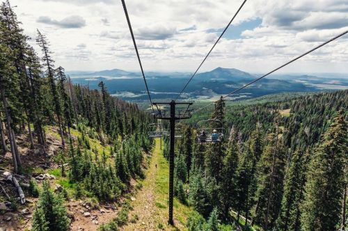 A scenic view from a chairlift, overlooking lush green trees and mountains under a cloudy sky.