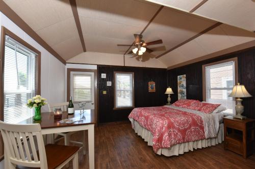 Cozy bedroom with a red floral bedspread, wooden accents, a dining table, and natural light from windows.