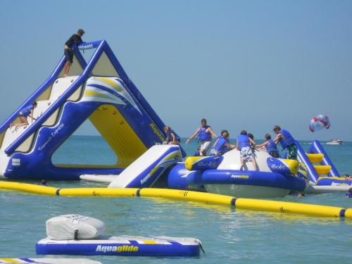 A colorful inflatable water park with people climbing and playing on various structures in a sunny beach setting.
