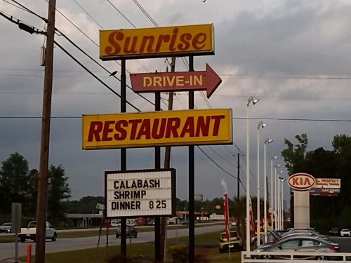Sign for Sunrise Drive-In Restaurant with a Calabash shrimp dinner special for $8.25, set against a cloudy sky.