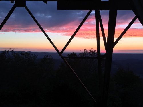 Silhouette of a structure against a vibrant sunset with pink and purple hues over distant mountains.