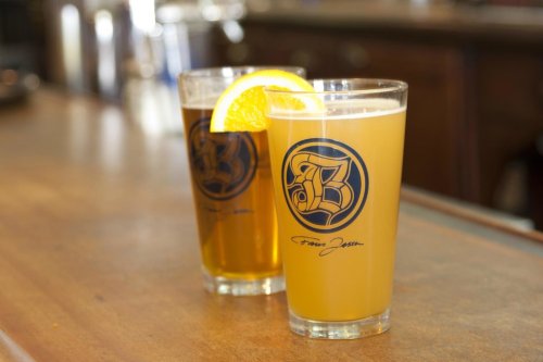 Two glasses of beer on a wooden bar, one light and one dark, each with a slice of lemon on the rim.
