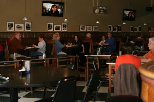 A cozy diner with patrons seated at tables, watching TV, and enjoying meals in a warm, inviting atmosphere.
