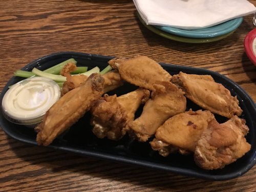 A platter of crispy fried chicken wings served with celery sticks and a side of dipping sauce.