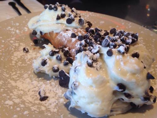 A plate of cannoli filled with creamy filling and topped with chocolate chips and powdered sugar.