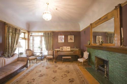 Cozy living room with vintage furniture, a piano, and a green-tiled fireplace, illuminated by a chandelier.