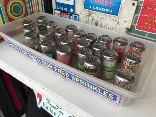 A tray of colorful sprinkle jars with various flavors, labeled "Have fun with our free sprinkles."