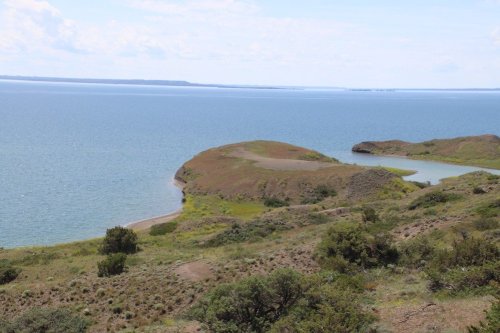 A scenic view of a calm lake surrounded by green hills and a clear blue sky.