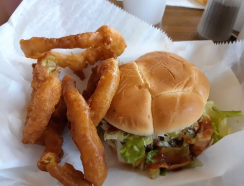 A hamburger with lettuce and sauce next to a serving of crispy onion rings on a white paper-lined plate.