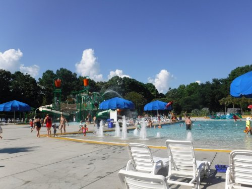 A sunny water park scene with a large pool, water slides, and families enjoying the day under blue skies.