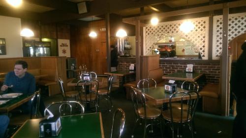 A cozy restaurant interior with wooden booths, green tables, and a counter in the background. A few patrons are seated.