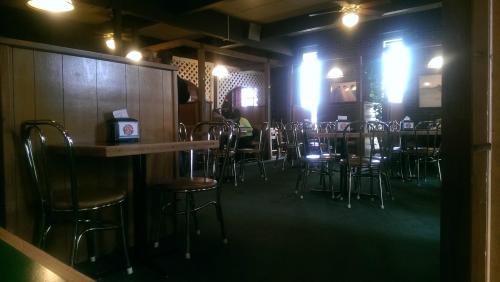 A nearly empty restaurant with wooden walls, metal chairs, and tables, featuring large windows and a cozy atmosphere.