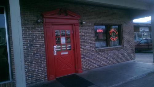 A red door with an "Open" sign, set against a brick wall, leading to a restaurant named "Tortilla Jack's."