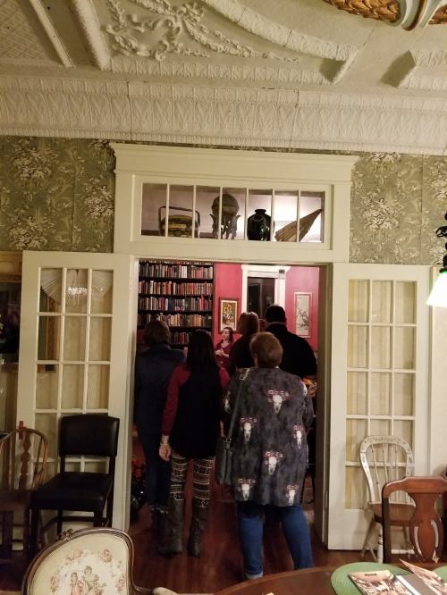 A group of people stands in a doorway, looking into a room filled with bookshelves and decorative walls.